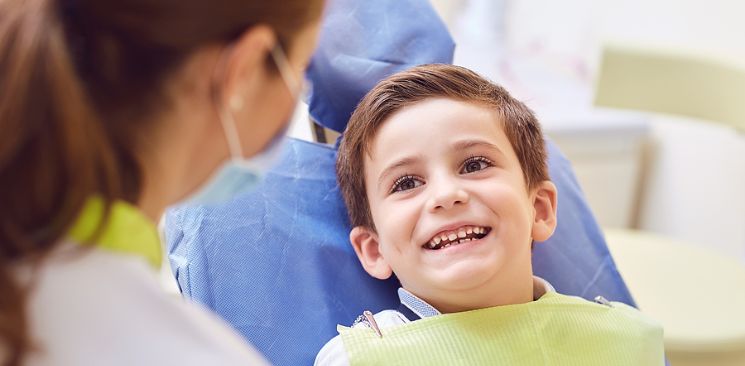 A boy on a dental chair is smiling at the dentist.