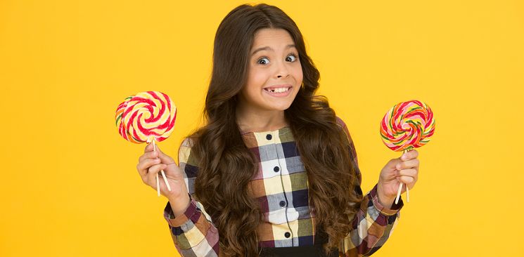 A Girl With Missing Tooth Is Holding Lollipops In Both Hands.