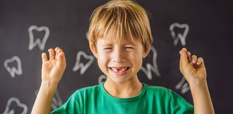 A boy smiling with missing teeth while holding loose tooth in each hand.