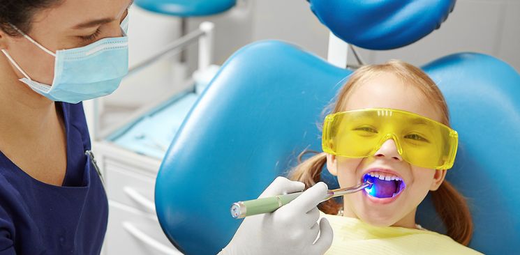 A little girl wearing yellow safety eye protection on a dental chair.