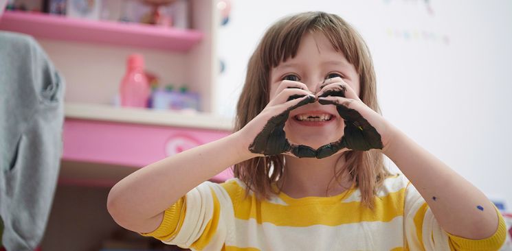 Little Girl With Missing Front Teeth Is Trying To Make A Heart Shape With Her Hands.