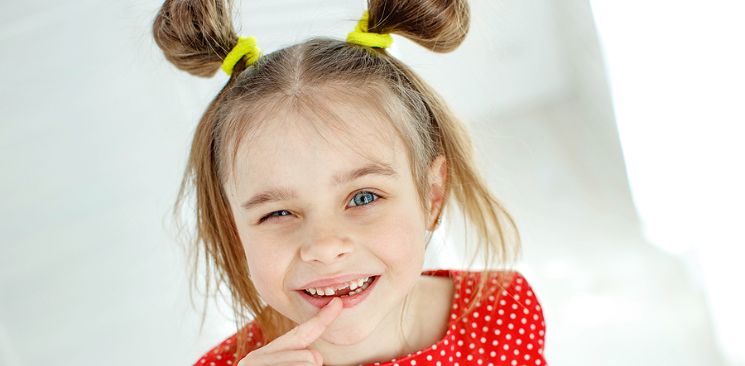 A little girl with pigtails is pointing at her missing front tooth.