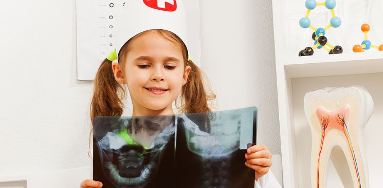 Young girl dressed as a dentist holding an x-ray.