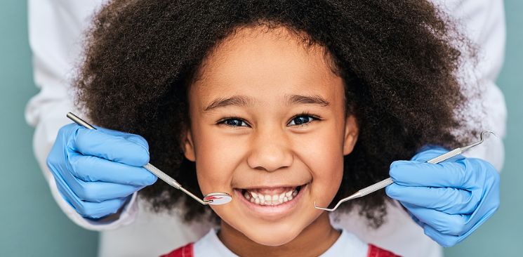 Young Girl Smiling While A Dentist Hold Tools From The Background.