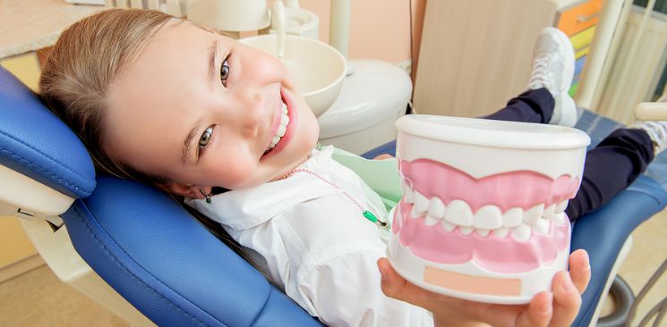 A smiling young patient showing off a model of teeth and gums.